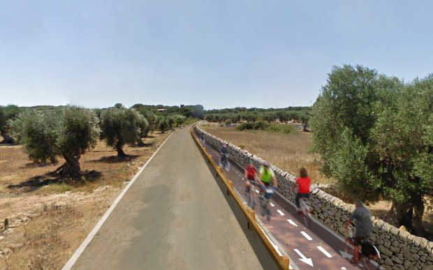 Fotoinserimento pista ciclabile di progetto delimitatta da parapetto di legno verso strada e muretto a secco verso il campo